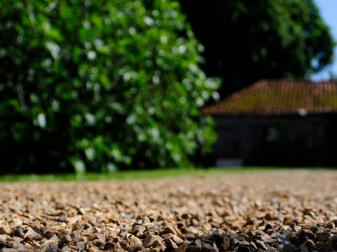 Close-up of gravel path with blurred building and green trees in background