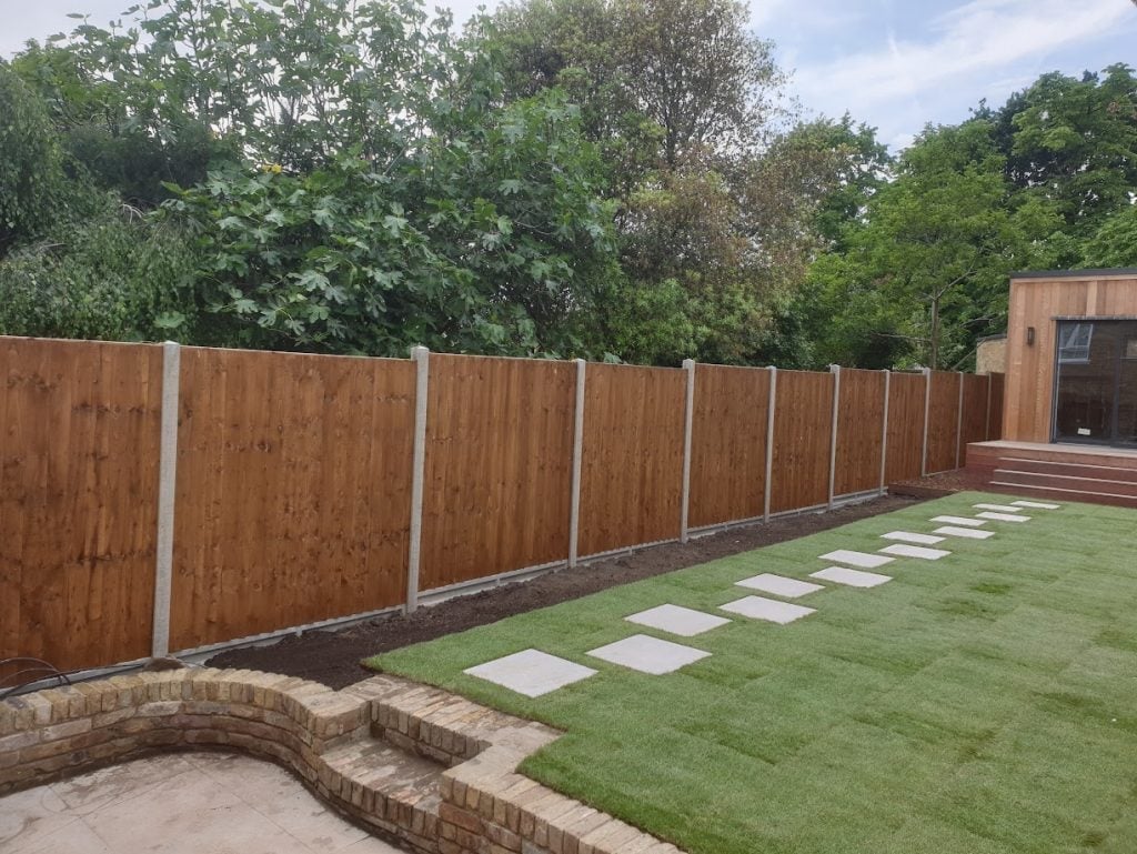 Backyard with wooden fence, manicured lawn, and stepping stone pathway with brick structure along the perimeter