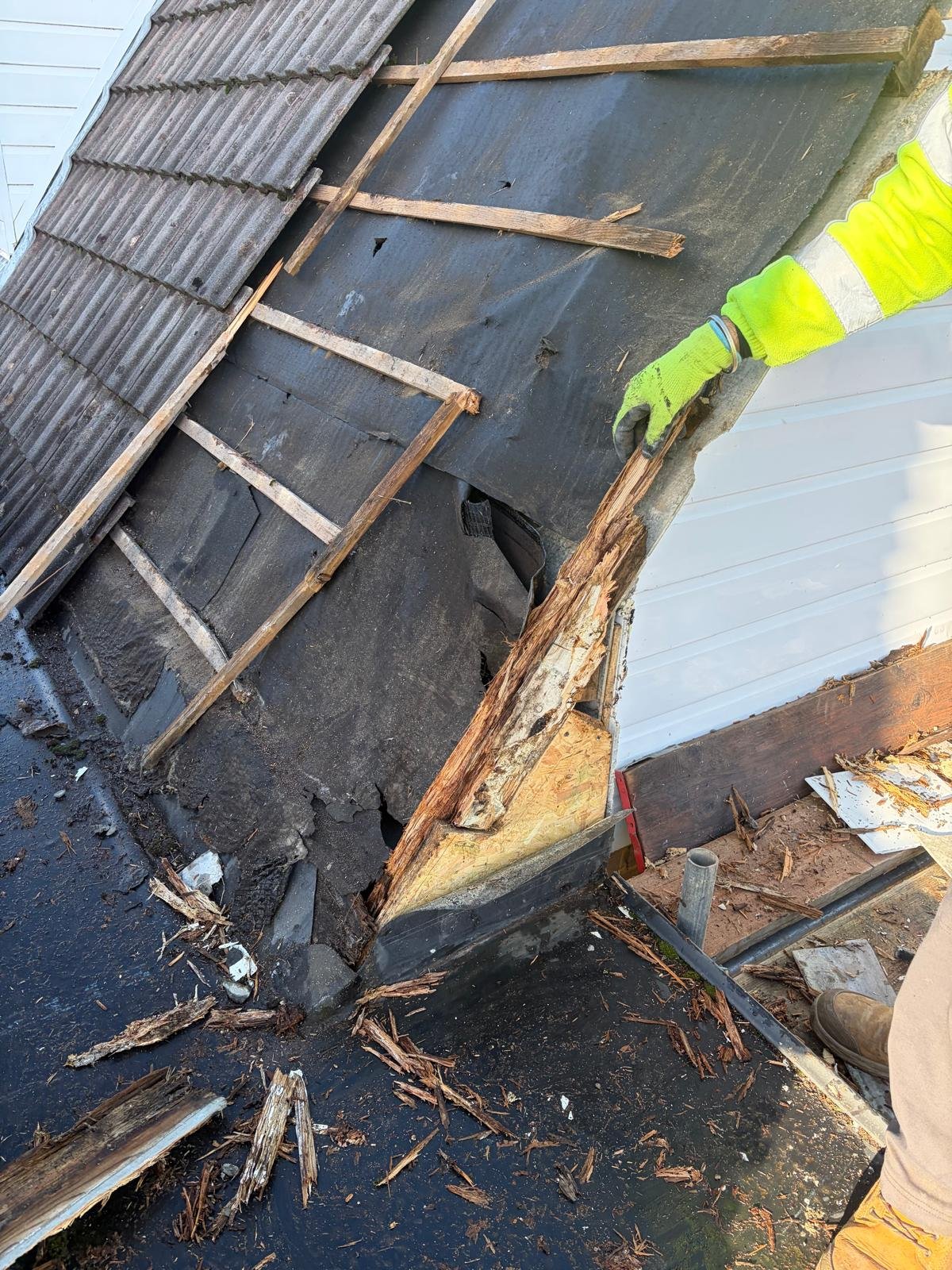 Worker in high-visibility vest inspecting deteriorating corrugated metal roof with rust and damage