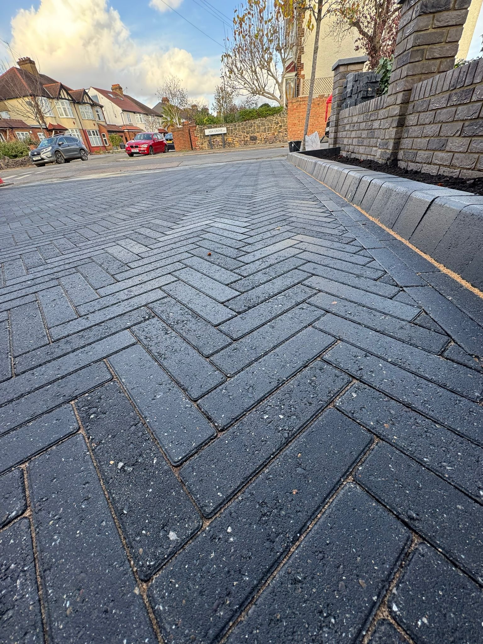 Newly laid dark patterned paver driveway with herringbone design in suburban residential area