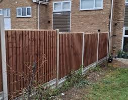 Red corrugated metal fence attached to brick house exterior with green lawn and bare bushes below