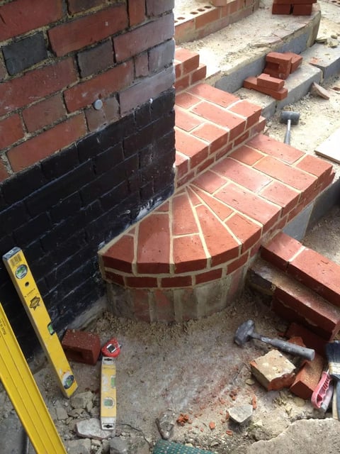 Curved red brick patio or steps under construction with level and tools on dusty ground