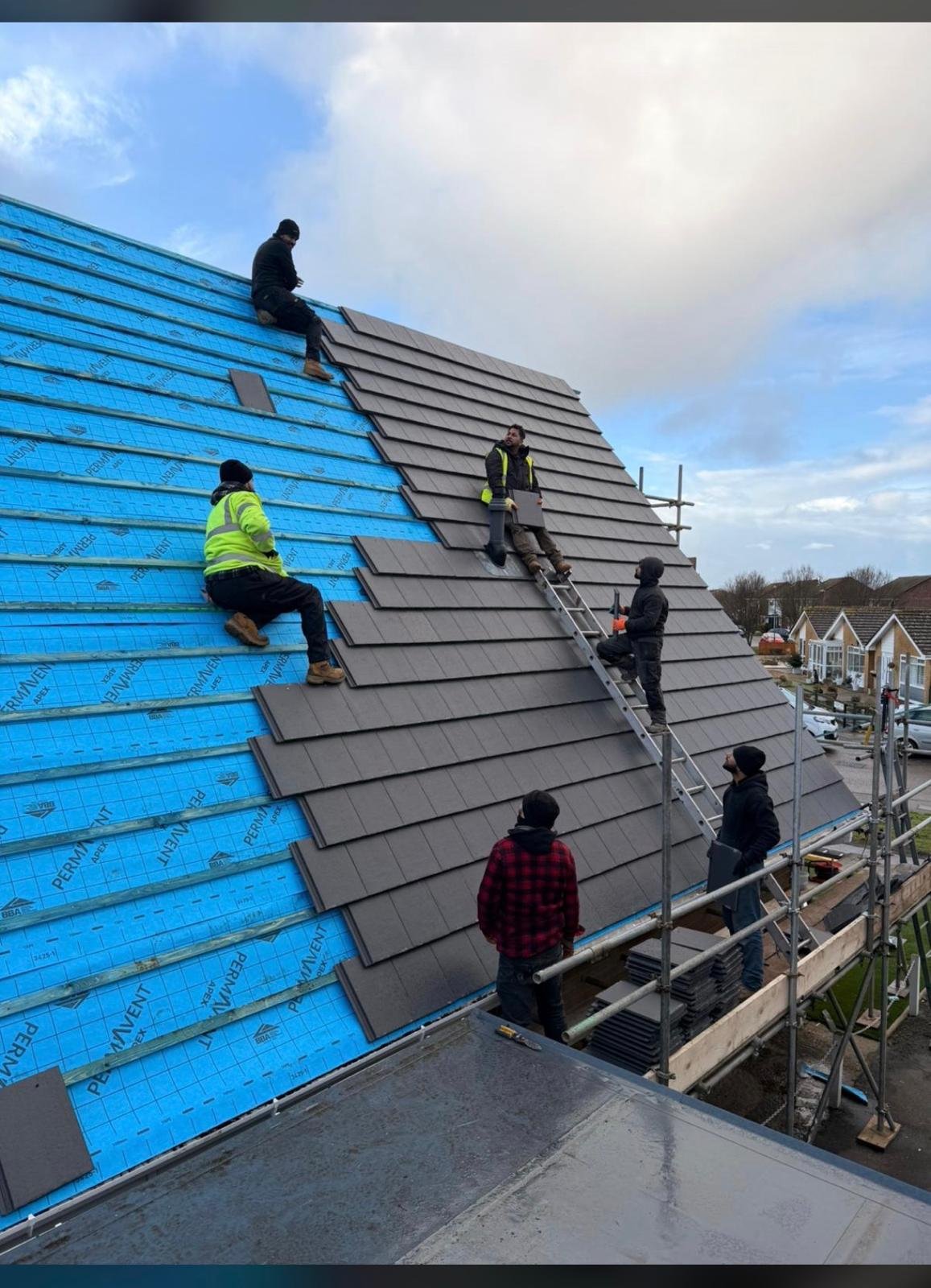 Construction workers installing roof tiles on a new residential building with blue weather protection and scaffolding visible