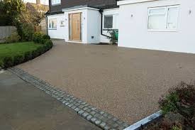 Modern house driveway with gray resin-bound surface bordered by decorative stone edging, green lawn visible on sides