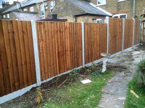 Wooden fence with white posts running along a residential garden path with brick townhouses visible in the background